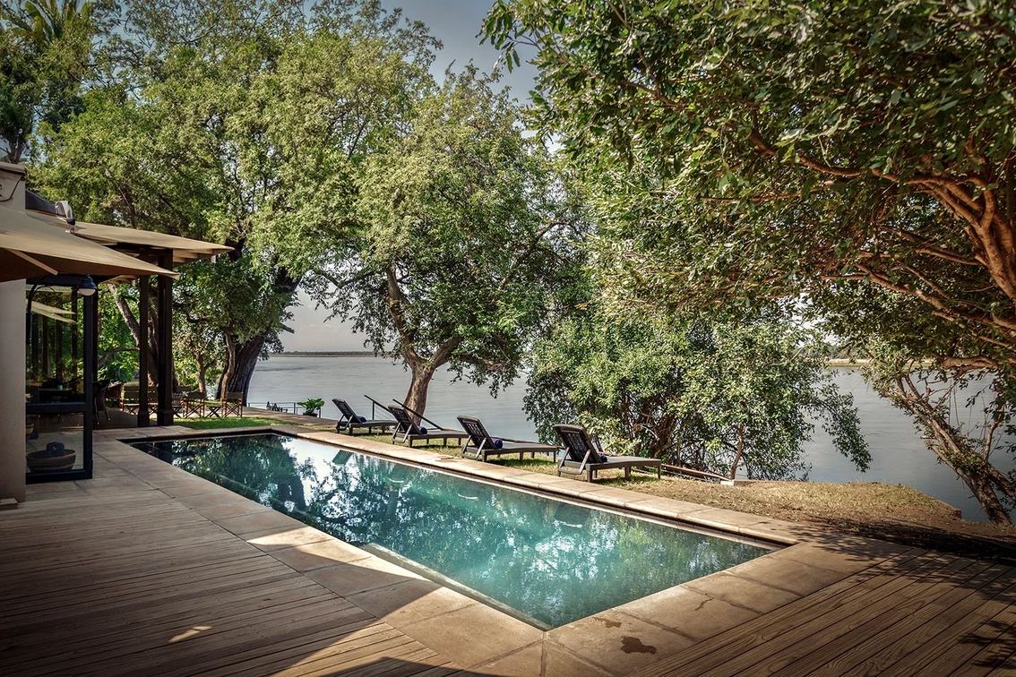 Ein Schwimmbecken und Liegen sitzen unter Bäumen am Flussufer im Baines' River Camp.