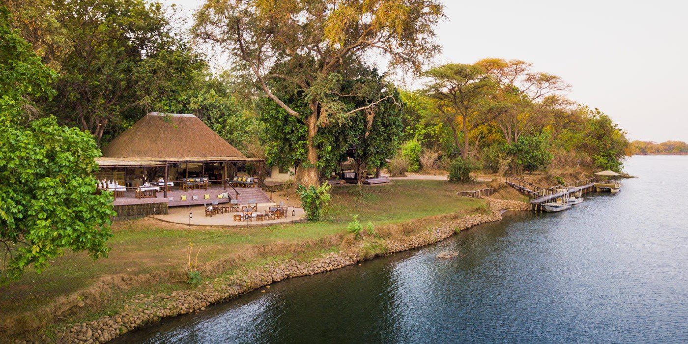 Das strohgedeckte Speisedeck und der Bootssteg am Flussgestade von Chiawa Camp in Lower Zambezi.
