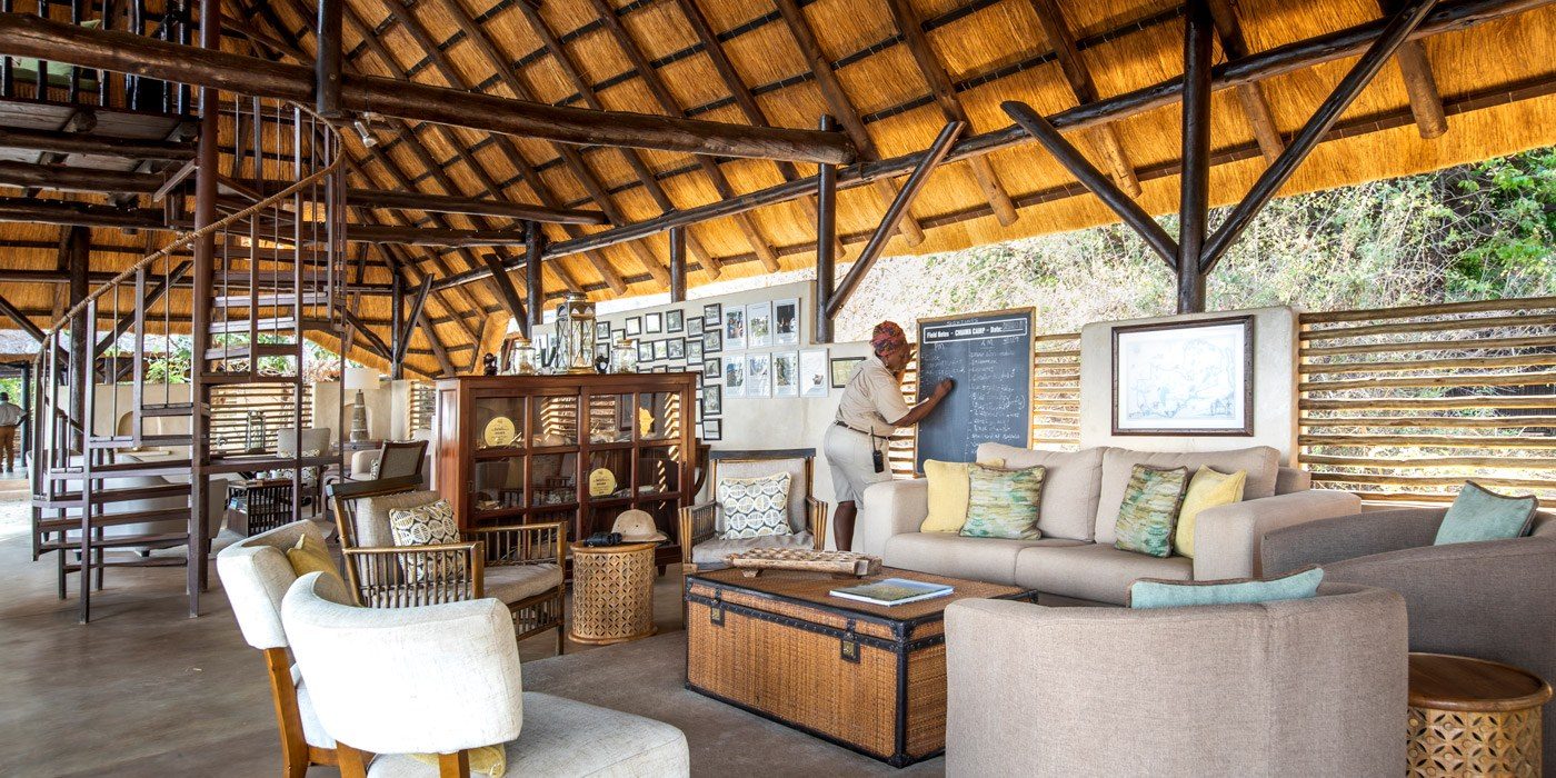 Die strohgedeckte Lounge im Chiawa Camp mit Sofas, einer Wendeltreppe und einer Tafel für Ranger-Feldnotizen.