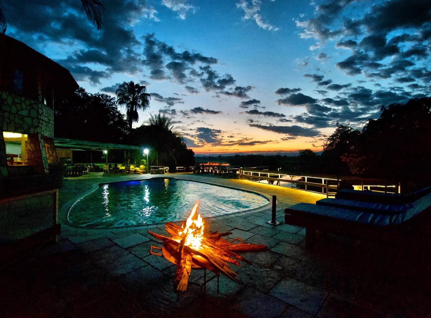 Un foyer brûle près de la piscine au crépuscule à Gwabi River Lodge en Lower Zambezi.