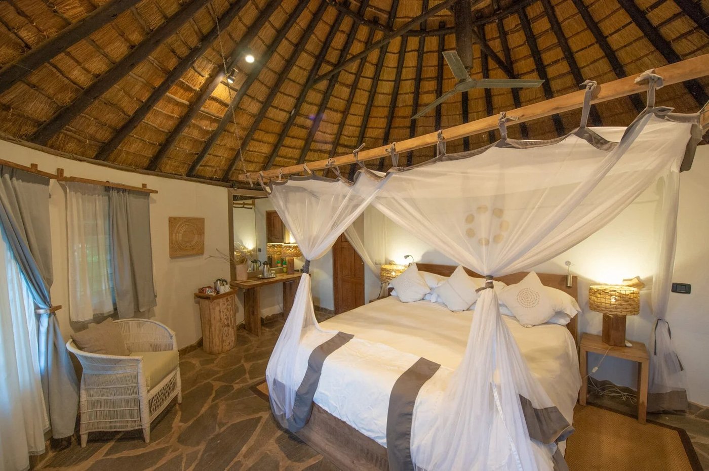 Ein Himmelbett mit Baldachin steht unter einem Strohdach in einem rustikalen Schlafzimmer in Kanyemba Lodge