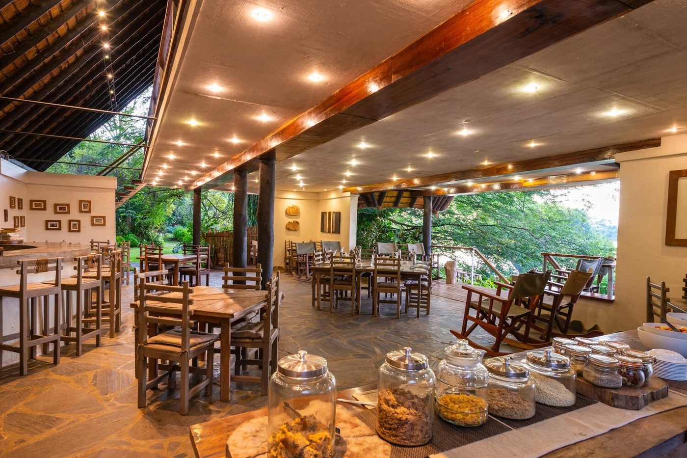 Holztische und warmes Licht erfüllen das offene Restaurant und die Bar in Kanyemba Lodge