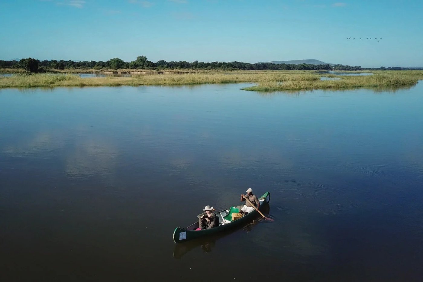 Ein Guide paddelt Gäste in einem Kanu über ruhiges Wasser nahe Kanyemba Lodge