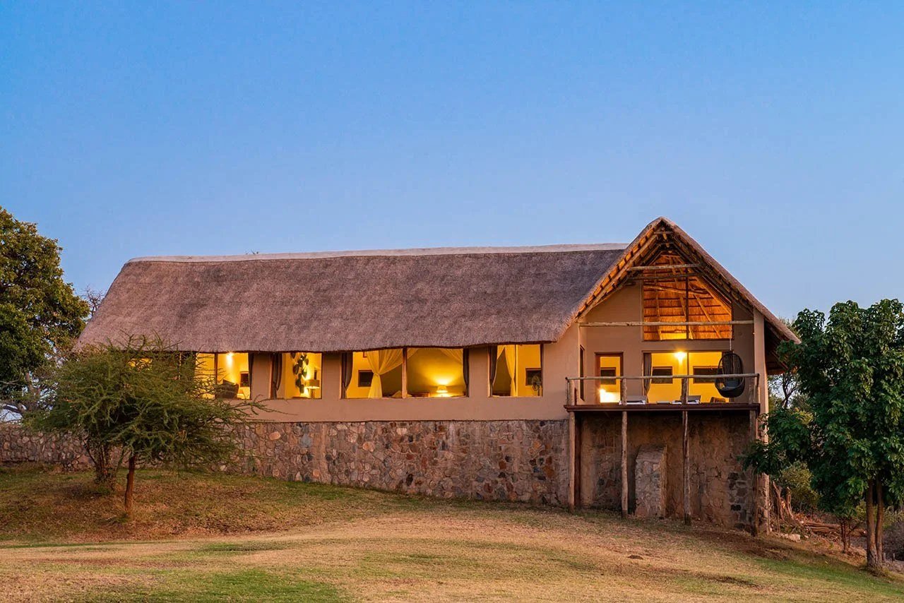 Le bâtiment en pierre au toit de chaume de Kayila Lodge parmi les arbres riverains de sa réserve privée dans le Lower Zambezi.