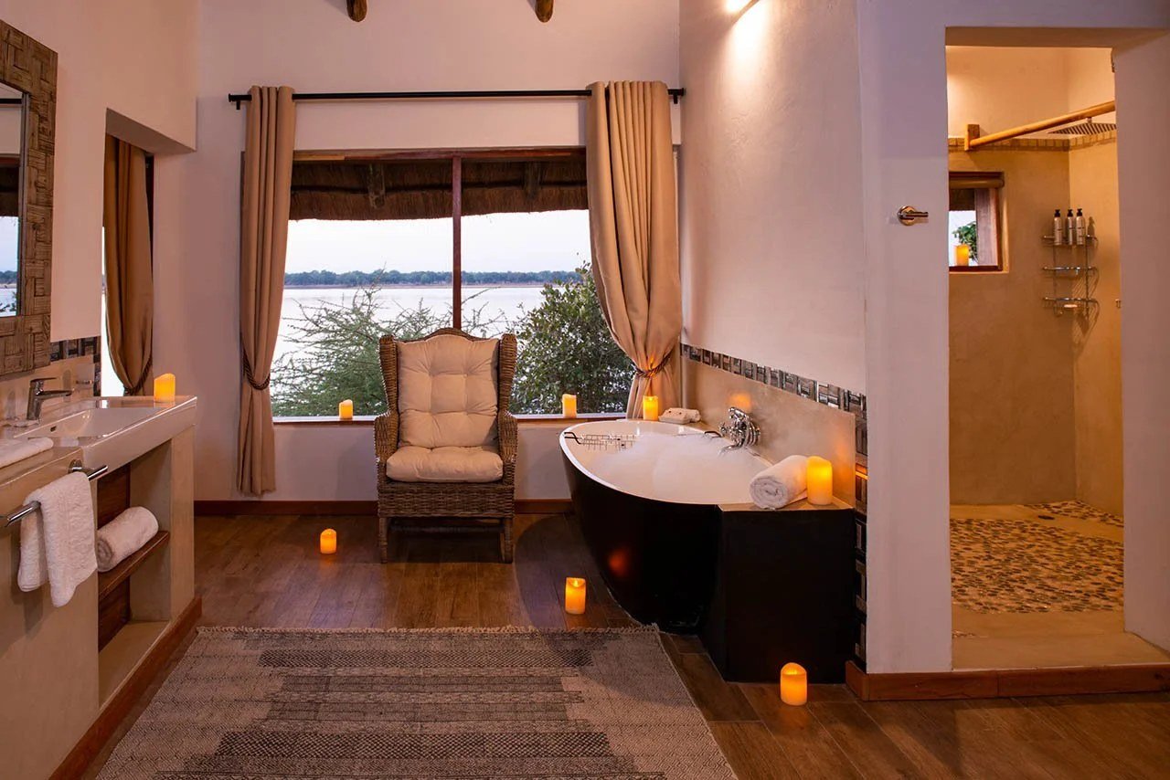 Eine freistehende Badewanne, beleuchtet von Kerzen, neben der begehbaren Dusche in Kayila Lodge