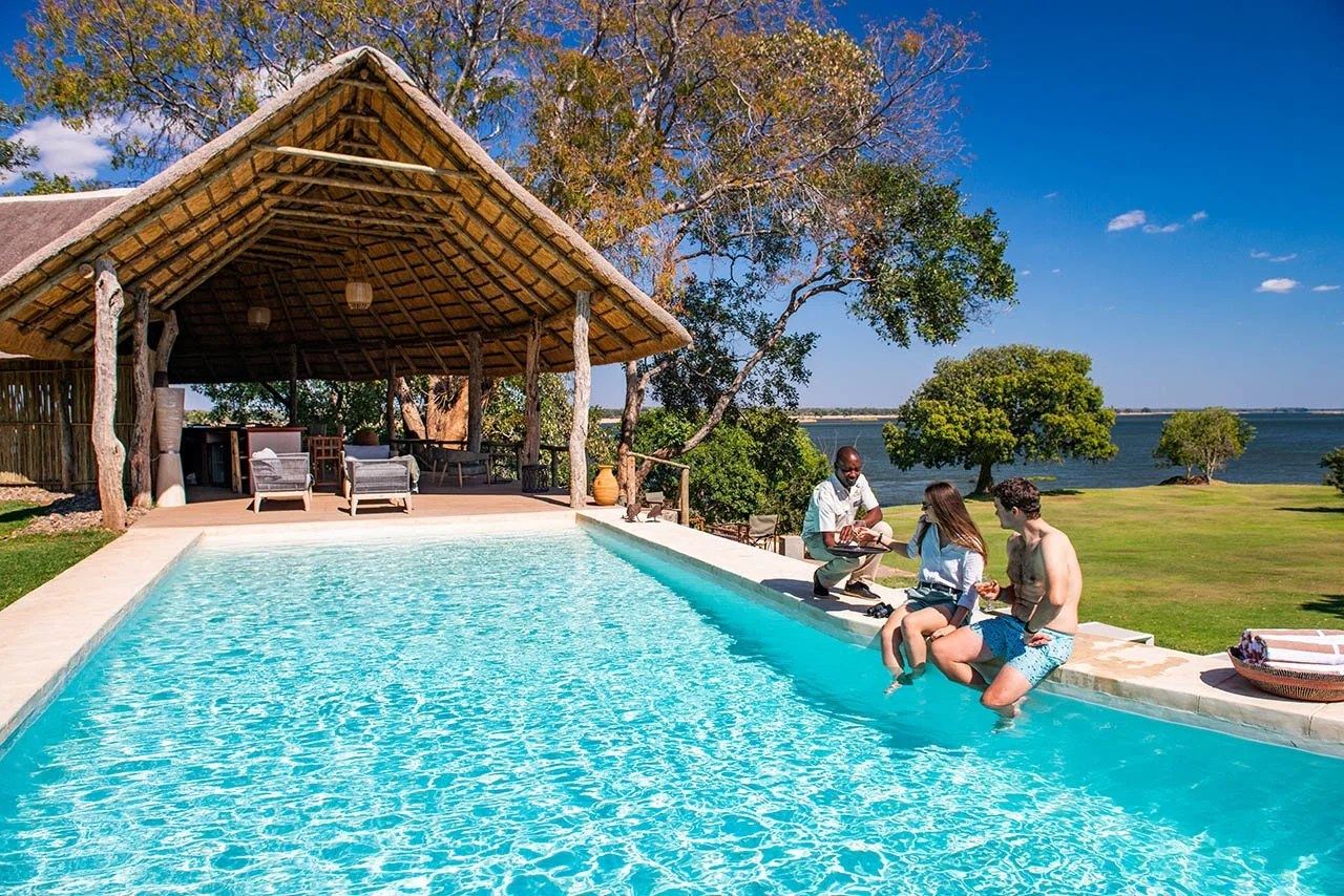 Gäste entspannen am Rand des Swimmingpools auf dem Rasen in Kayila Lodge