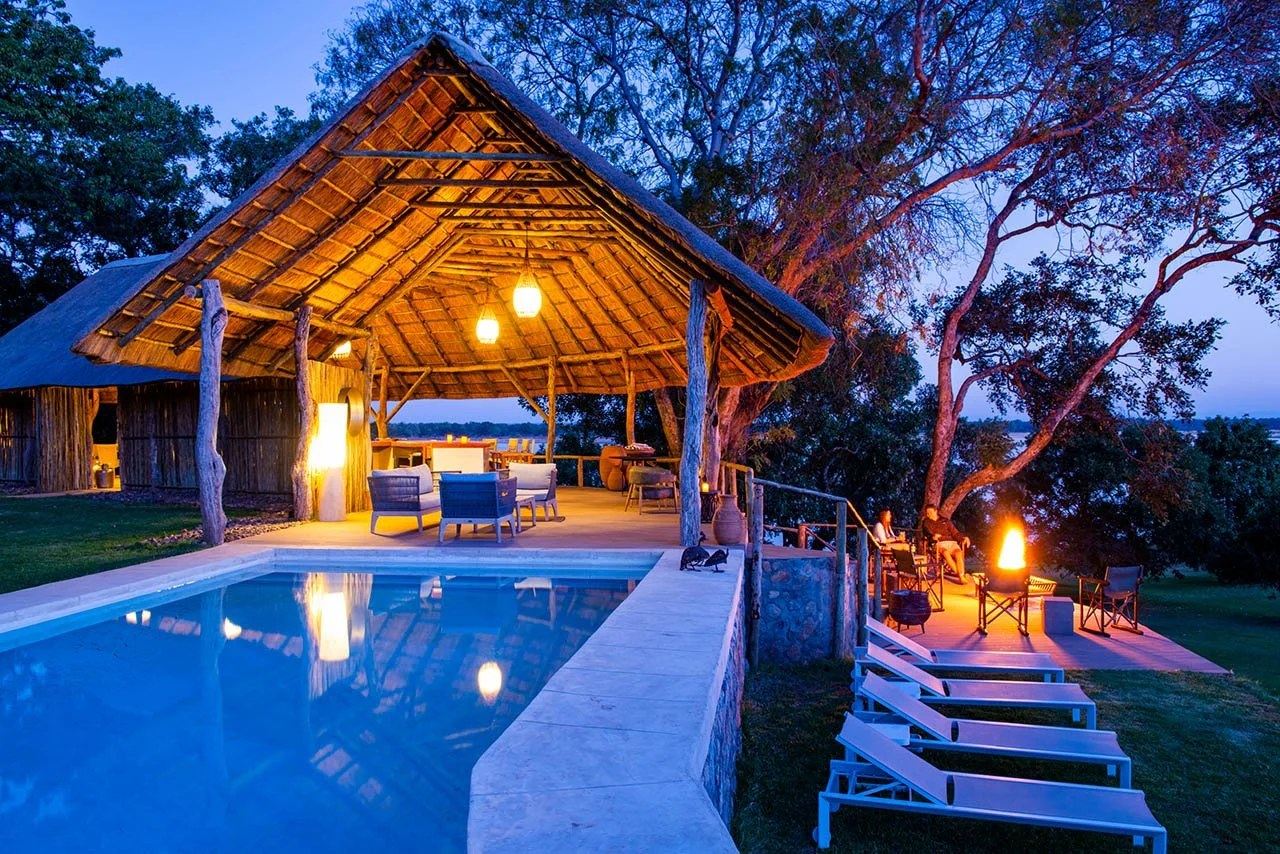 Liegen und eine Feuerstelle umgeben den Pool bei Einbruch der Dämmerung in Kayila Lodge