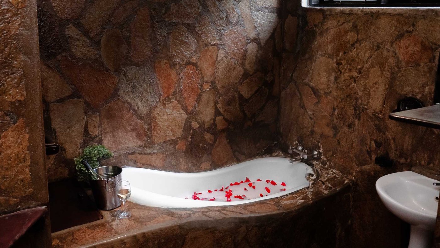 Eine Steinbadewanne mit Rosenblättern steht in einem rustikalen Badezimmer in Kiambi Safari Lodge.