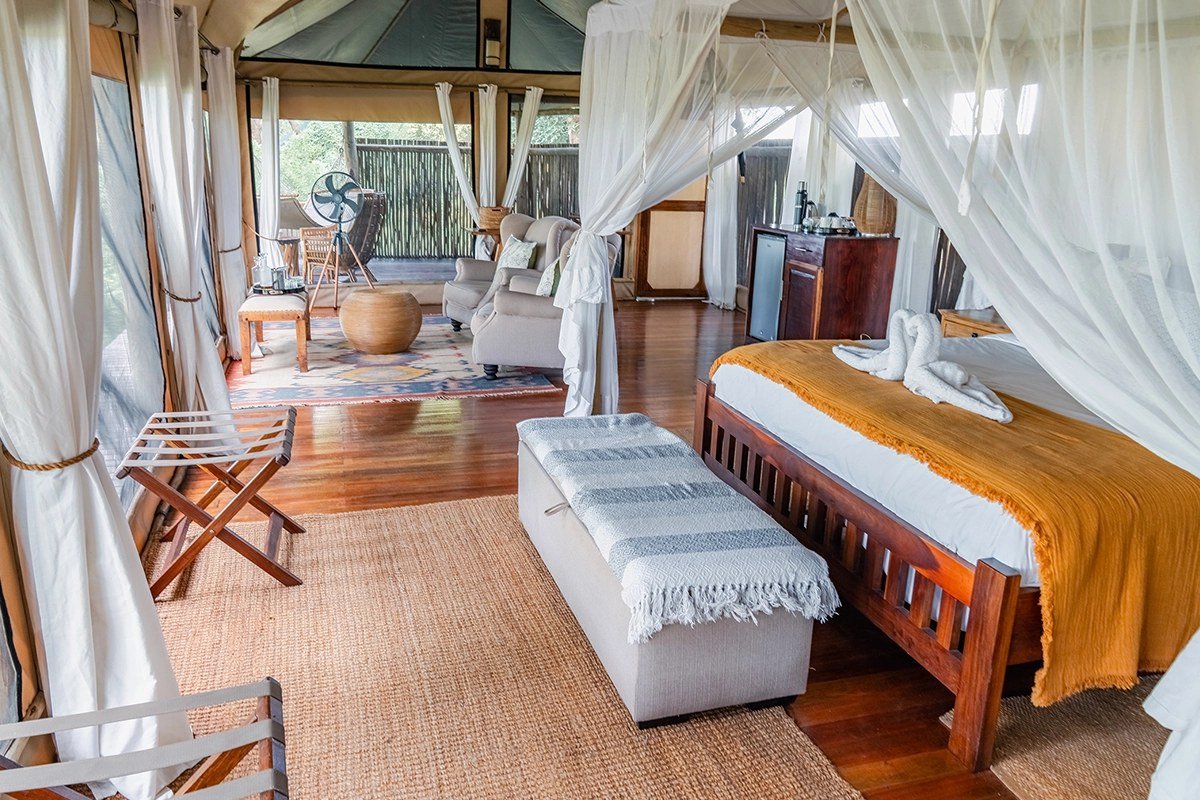 Een hemelbed en loungestoelen vullen een openzidig tent bij Muchichili Safari House.