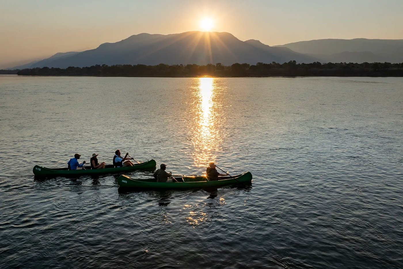 Gidsen en gasten pagaaien twee kano's over de Zambezi bij zonsondergang in de buurt van Muchichili Safari House.