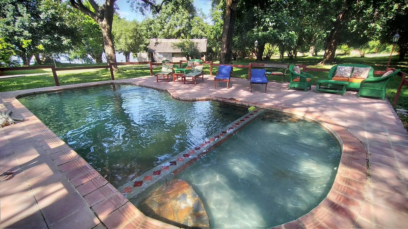 Sonnenliegen säumen den Swimmingpool auf dem Rasen in Mvuu Lodge
