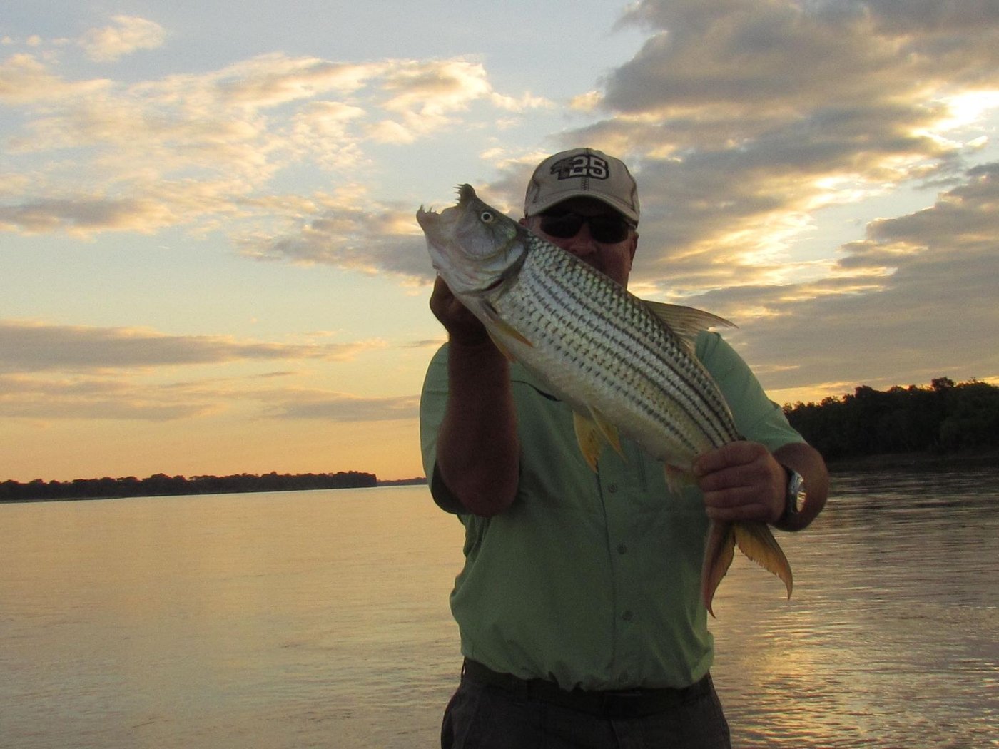 Ein Gast präsentiert seinen Tigerfisch-Fang bei Sonnenuntergang neben Mvuu Lodge
