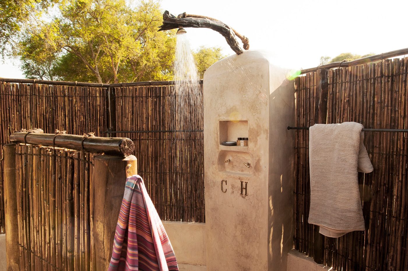 Une douche en plein air avec une clôture en roseau et des serviettes rayées à Old Mondoro.