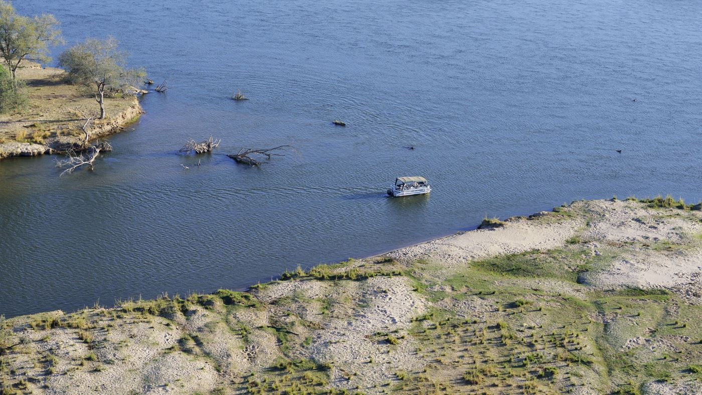 Luftaufnahme eines Bootes auf dem Zambezi an einer Sandbank vorbei in der Nähe von Potato Bush Camp.