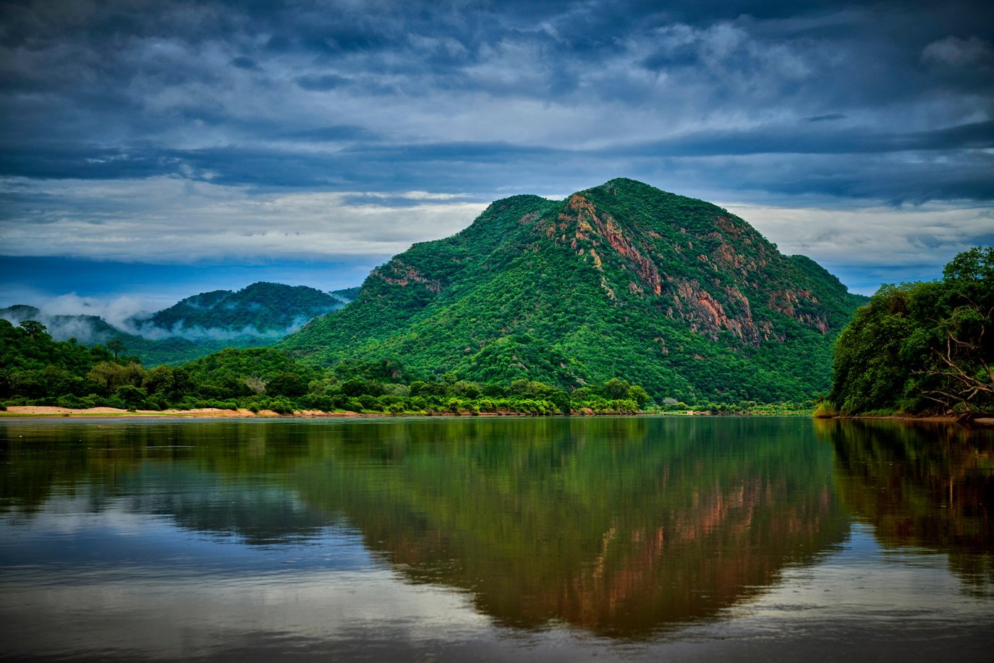 Les falaises boisées de la Gorge Mpata se reflètent dans l'eau calme à l'aube près de Redcliff Zambezi Lodge.