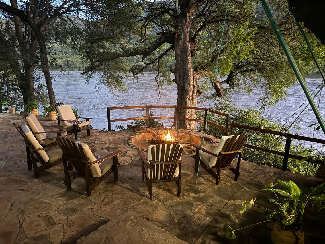 Des chaises en osier entourent un foyer sur la terrasse sous un arbre à Redcliff Zambezi Lodge.