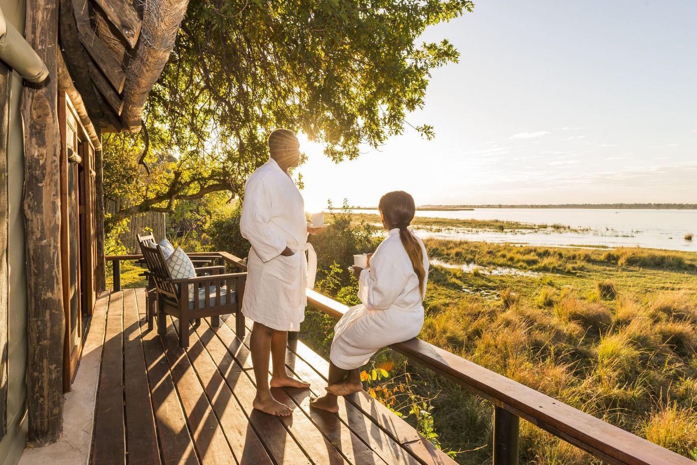 Des clients en peignoir regardent le coucher de soleil sur la plaine inondable depuis la terrasse de Royal Zambezi Lodge.