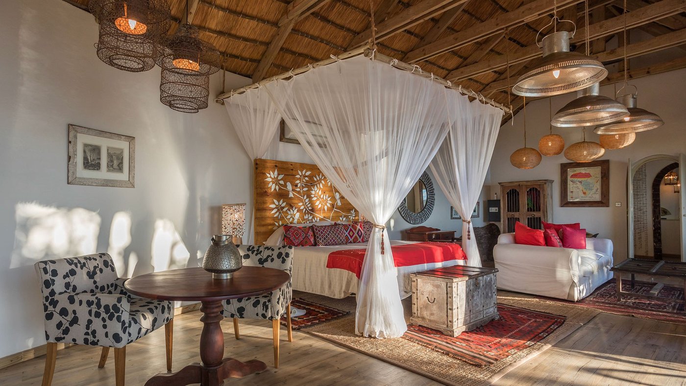 Ein vier Meter hohes Bett mit Moskitonetz drapiert in einer strohgedeckten Suite im Sausage Tree Camp.