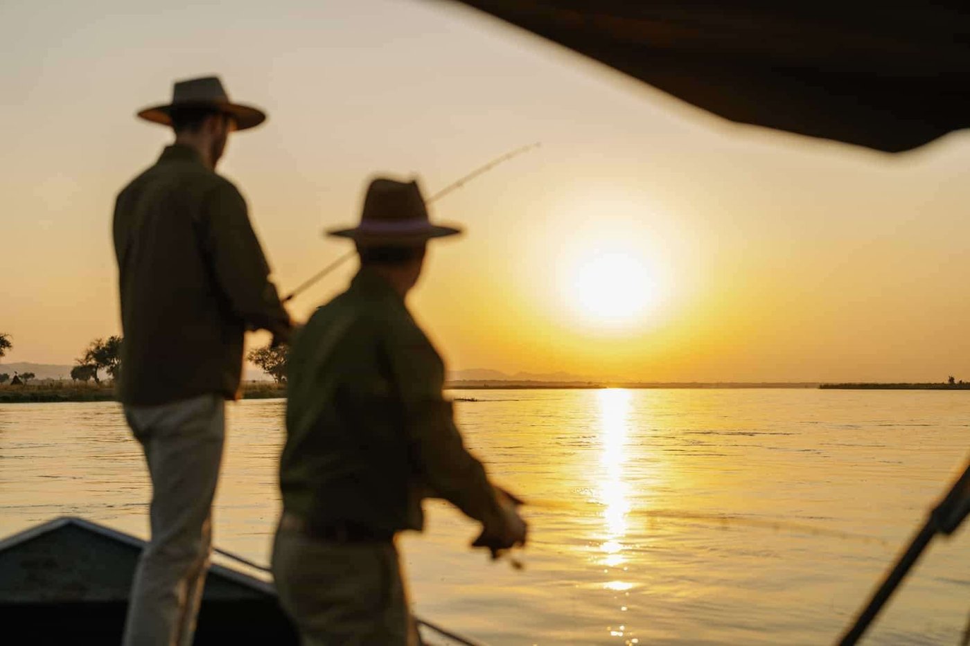 Deux pêcheurs lancent des mouches depuis le bateau au coucher du soleil près du camp Time and Tide Chongwe.