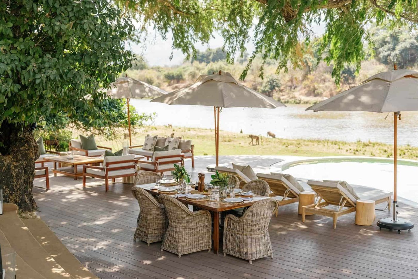 Von Sonnenschirmen beschattete Tische säumen das Deck mit Blick auf den Fluss bei Time and Tide Chongwe House.