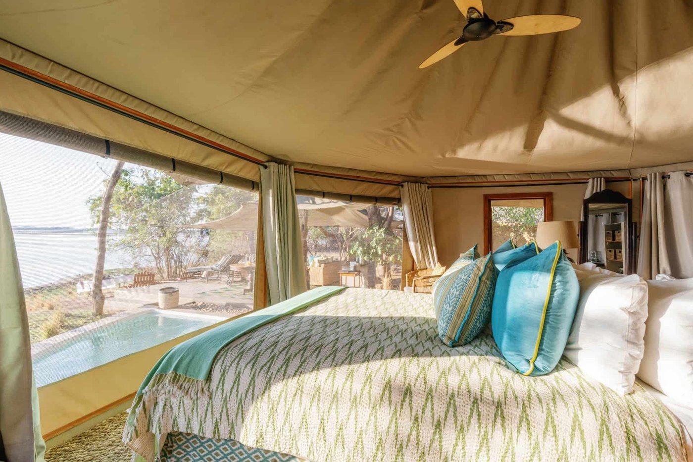 Ein blaugrün akzentuiertes Bett und ein Sessel blicken auf den privaten Pool bei Time and Tide Chongwe Suites.