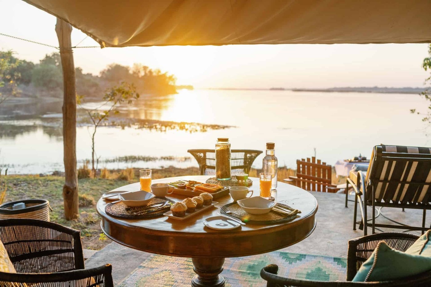 Das Frühstück wird auf einem Tisch am Fluss bei Sonnenaufgang bei Time and Tide Chongwe Suites angerichtet.