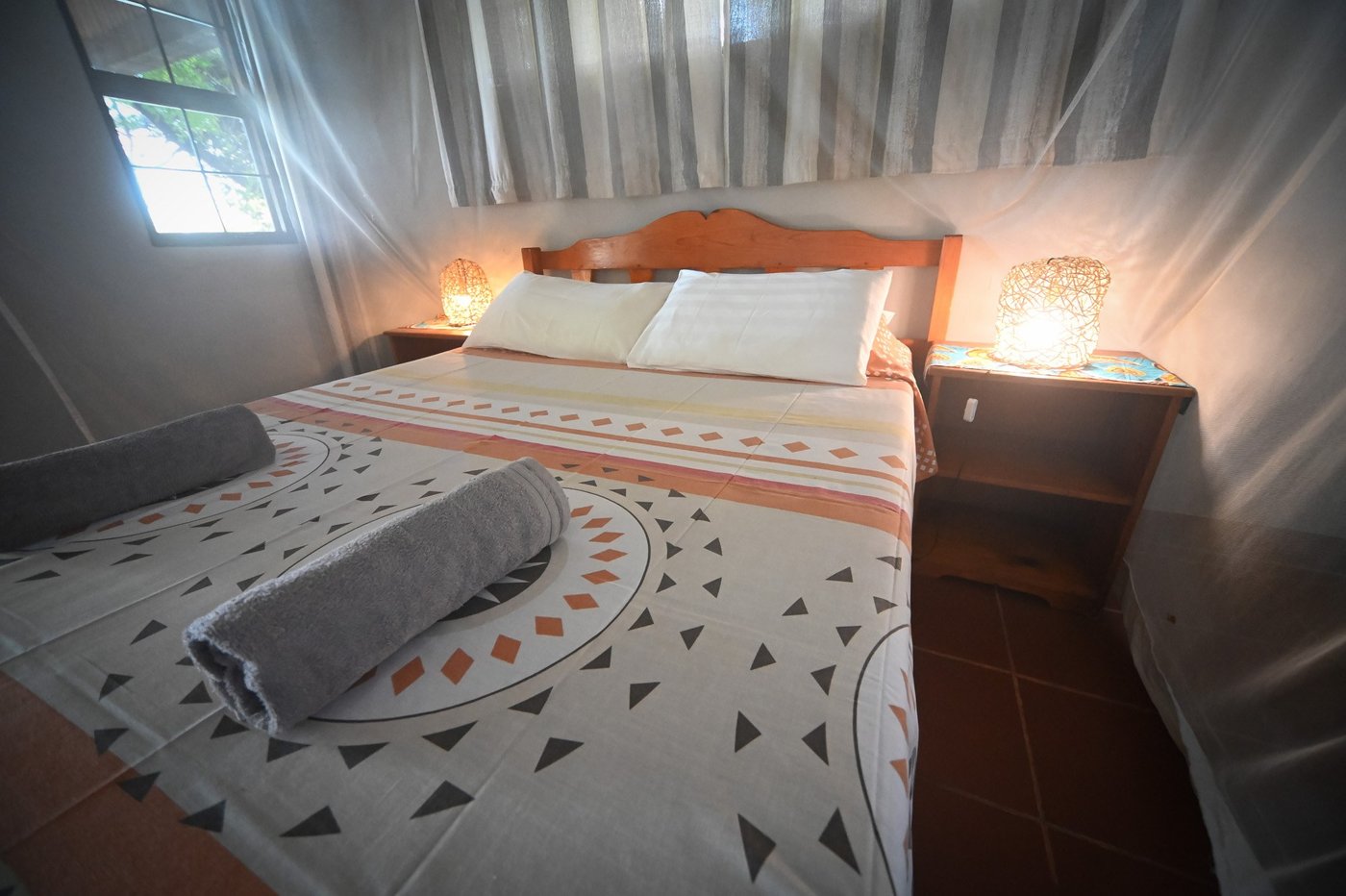 Een gemusterde sprei en bedside lampen voorzien een eenvoudige kamer bij Wildtracks Lodge.