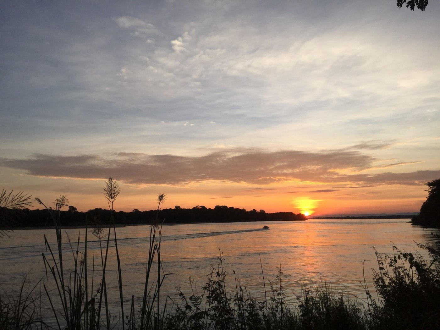 Een boot steekt de rivier over bij zonsondergang in de buurt van Wildtracks Lodge.