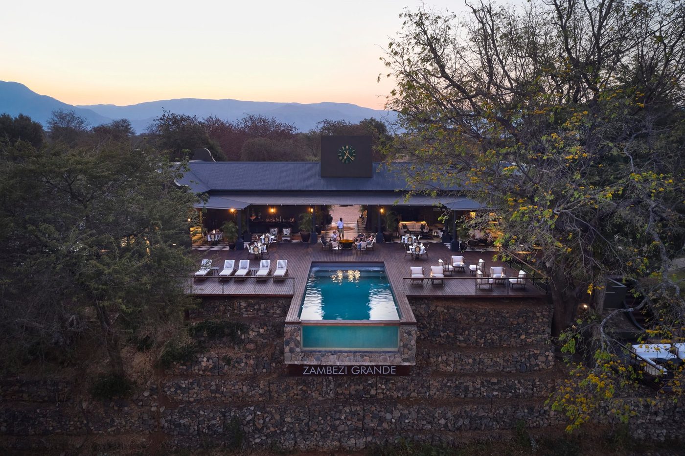 La terrasse piscine et le salon de Zambezi Grande surplombent la rivière avec les montagnes derrière à Lower Zambezi.